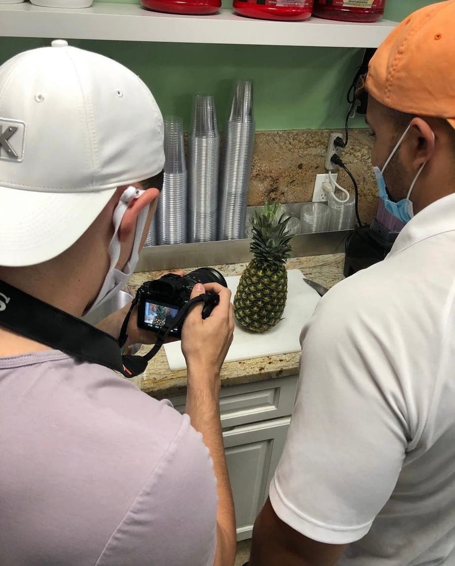 A MediaScher videographer in a face mask filming a pineapple on a counter for a small local business
